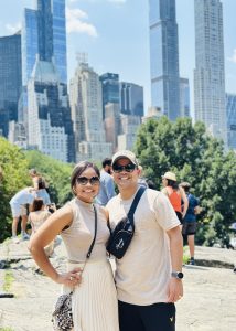 Smiling couple in Central Park on a beautiful summer day with the skyline of Central Park South behind them