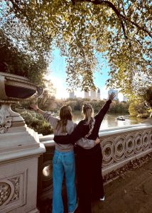 Two girls hugging on Bow Bridge in Central Park, looking out over the lake on a beautiful afternoon