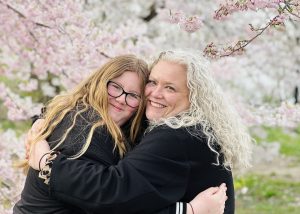 Smiling mother and daughter hugging in front of cherry blossoms in Central Park during a spring pedicab tour