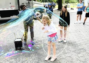 Young girl laughing inside a giant bubble while her older sister watches in the Central Park Mall during a pedicab tour