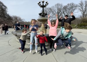 Parents and kids jumping in front of Cherry Hill Fountain during a Central Park pedicab tour, all smiles and having a blast