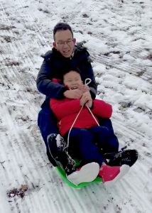 Father and son sledding together for the first time in Central Park, laughing as they ride down a snowy hill during a pedicab tour