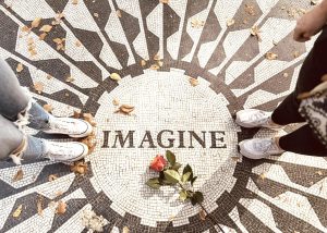 Two pairs of feet standing on opposite sides of the ‘Imagine’ mosaic at Strawberry Fields