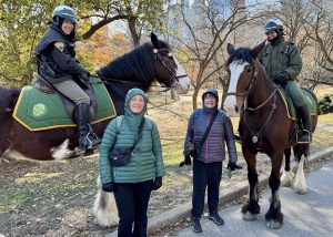 Two visitors posing with mounted Park Rangers and their horses on a chilly day in Central Park, all smiling