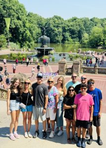 Family of 10 posing on Bethesda Terrace steps in front of the Angel of the Waters fountain on a sunny summer day
