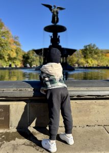 Child gazing up at the Angel of the Waters in Central Park with his back to the camera